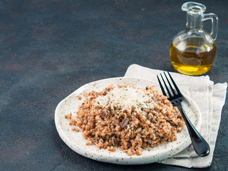 Buckwheat risotto with dried mushrooms in craft plate on black cement background. Gluten-free and vegetarian buckwheat recipe ideas. Copy space