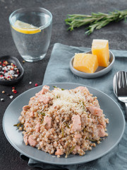 Raw buckwheat risotto with chicken meat and rosemary served parmesan cheese in gray plate on black cement background. Gluten-free and buckwheat recipe ideas. Copy space