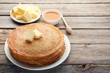 Heap of pancakes with butter and honey on wooden table