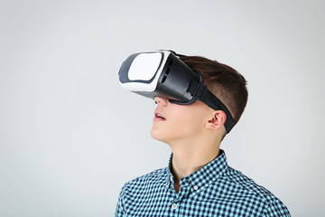 Young boy in virtual reality goggles on grey background
