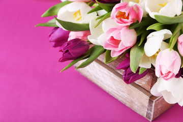 Bouquet of tulips in crate on pink background
