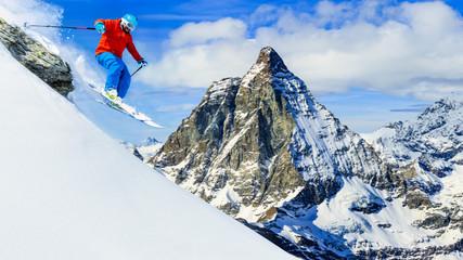 Man jumping from the rock, skiing on fresh powder snow with Matterhorn in background, Zermatt in...