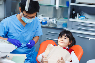 Little girl is sitting still in the dentist chair, smiling and showing thumbs up. Doctor and his young cheerful patient. Pediatric dentistry, introduction to dentistry, prevention dentistry concept