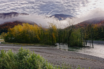 River bank, autumn forest and mountains in clouds and fog, Sochi region, Russia
