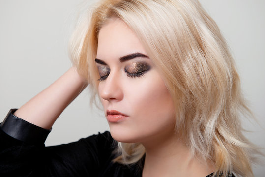 Blonde woman with bright makeup on the eyes closed and the hand in her hair on white isolate closeup