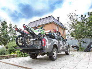 Two dirt bike motorcycles on the back of the camo truck on the driveway.