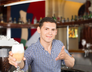 Handsome young smiling bartender serving a glass of tasty cocktail in the restaurant setting.