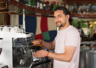 Handsome young smiling male barista preparing coffee drink using coffee machine.