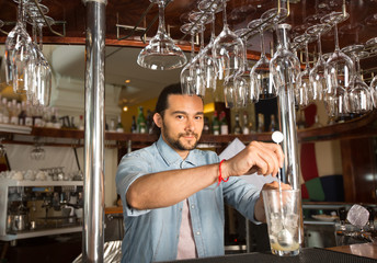 Handsome young smiling bartender holding steel swizzle spoon in the glass with ice.