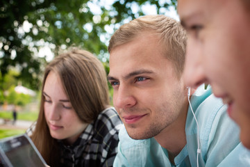Fototapeta premium Smiling young thoughtful guy relaxing outdoors and listening to music surrounded by his friends.