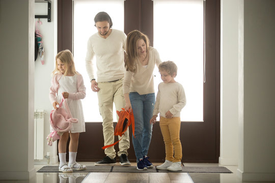 Children siblings returning sweet home with parents, happy family of four coming back to house after walking together from school or work, father mother and two kids son daughter standing in hall