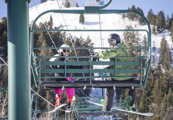 Smiling father and daughter riding a chair lift together on a sunny day at a ski resort - Powered by Adobe