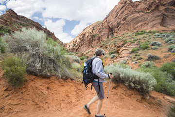 Active senior woman hiking in a red rock sandstone canyon. The healthy, retired woman is enjoying a walk along a scenic trail with vibrant red rock cliffs in the background