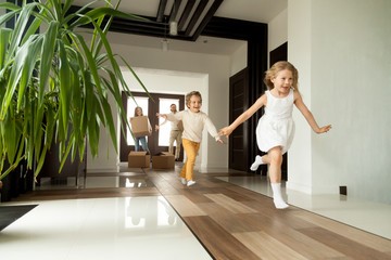 Happy young family with cardboard boxes in new home at moving day concept, excited children running into big modern own house hallway, parents with belongings at background, mortgage loan, relocation - obrazy, fototapety, plakaty