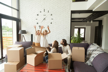 Happy married couple with kids playing while packing unpacking in modern living room interior, cheerful family and children having fun with boxes on couch together at moving day, move in out new home
