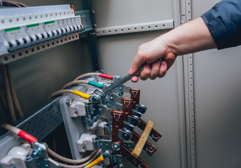 Electricians hands testing switches in electric box. Electrical panel with fuses and contactors