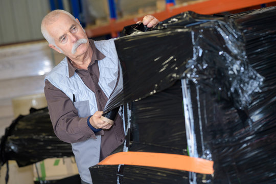 Elder Worker Using Shrink Wrap To Pack Items In Warehouse