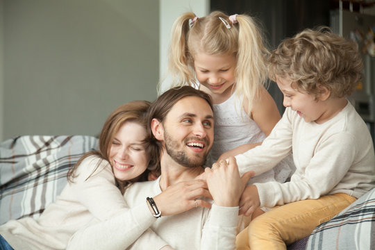 Cheerful parents and little children laughing having fun at home, wife with kids embracing hugging husband showing dad love, care and support, cozy loving family of four together, happy fathers day