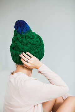 Young woman in warm hand knitted hat at home. Pretty lady in big green cap, smiling happily. Turn away from camera. Vertical shot.