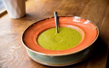 Close up of tasty delicious green pea soup of in big pink rounded plate on wooden table. Homemade dish cooked at kitchen. Stylish interior.
