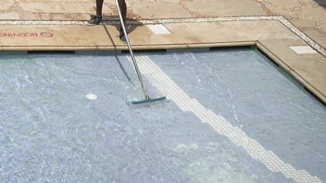 Worker cleans the water pool with brush. Cleaning public waterpools is required to keep it safe and sanitary hygienic service.