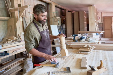 Portrait of mature bearded carpenter carving beautiful  wooden stair post in modern workshop, copy space