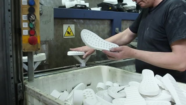 Slow motion of a worker puts the soles on the painting conveyor