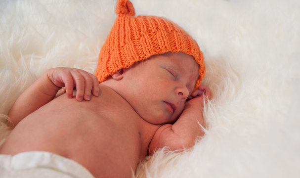 cute newborn baby in knitted orange hat cap