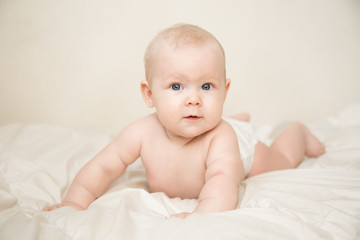 Beautiful smiling cute blonde baby girl with blue eyes lying  on the bed in the room. Happy child