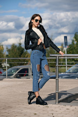 fashionable young woman in rock style clothes, black leather jacket, blue jeans, tights in a grid under battered jeans