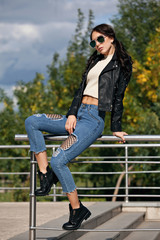 Obraz na płótnie Canvas fashionable young woman in rock style clothes, black leather jacket, blue jeans, tights in a grid under battered jeans