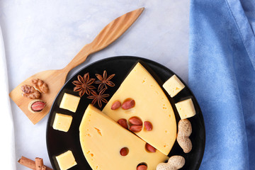 Hard cheese, cheese with holes on a black plate, cheese with honey on a white background, slices of cheese with nuts on a light background, Christmas dinner with cheese, honey and nuts, cinnamon stick