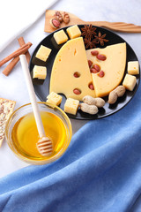 Hard cheese, cheese with holes on a black plate, cheese with honey on a white background, slices of cheese with nuts on a light background, Christmas dinner with cheese, honey and nuts, cinnamon stick