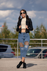fashionable young woman in rock style clothes, black leather jacket, blue jeans, tights in a grid under battered jeans