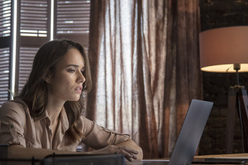 Young business woman sitting with floor lamp at table and looking laptop