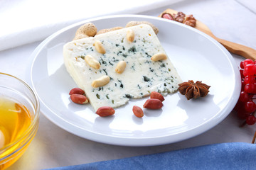 Cheese with a mold on a white plate, honey, nuts, red berries on a white background, soft cheese with nuts for Christmas dinner, minimalism