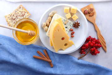 Cheese with mold and hard yellow cheese on a white plate, honey, nuts, red berries on a white background, cheese with holes for Christmas dinner, cheese background