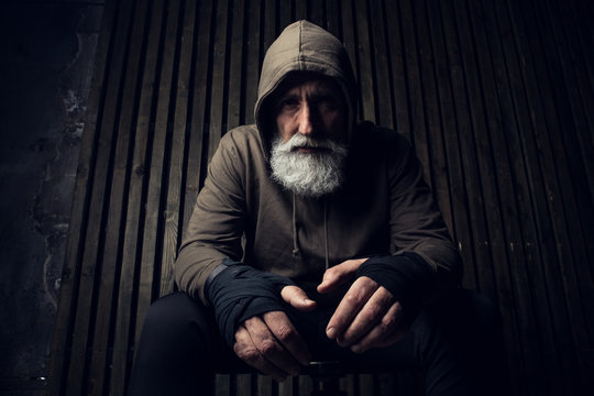 Serious bearded man ready to fight. Sport and fit man in hood sit on a chair. Workout and box sport. Extreme sport for old man. Close up portrait of man hands over his sports bandages