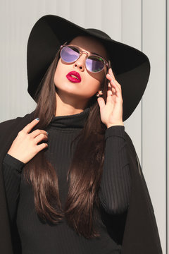 Closeup portrait of luxury young woman with shiny hair, wears hat and glasses, posing in sun light
