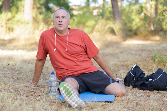 middle age sitting runner outside doing stretch in forest
