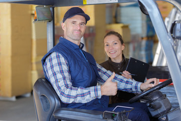 forklift driver and female supervisor with clipboard at warehouse