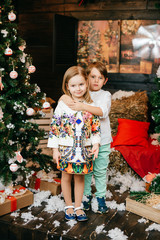 Boy and girl in love. Christmas tree and new year decorations. Lovely little kids hugging each other. Winter holidays. Young male and female playing and laughing in studio. Children joyful emotions.