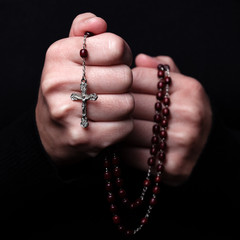 Female hands praying holding a rosary with Jesus Christ in the cross or Crucifix on black background. Woman with Christian Catholic religious faith