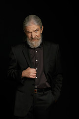 Aged beardy man with severe look. Old male in studio standing against black background.