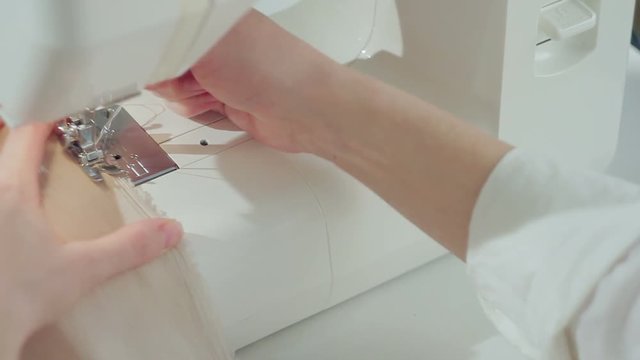 Closeup of a fashion designer woman sews on a sewing-machine an evening silk dress