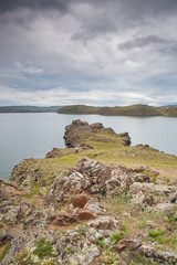 Rocky shore of lake Baikal. Rocks overgrown with grass near the water. Rain clouds in the lake. For...