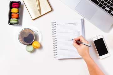 Feminine workspace with empty ruled notebook, hand writting in it, coffee, phone and laptop keyboard on white table