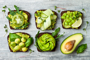 Fresh avocado toasts with different toppings. Healthy vegetarian breakfast with rye wholegrain sandwiches - obrazy, fototapety, plakaty