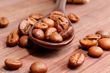 Grains of coffee close-up. Coffee beans are located on a spoon among the wooden texture. Coffee grains are located on a spoon on a wooden. Java composition from whole grains of coffee.