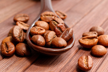 Grains of coffee close-up. Coffee beans are located on a spoon among the wooden texture. Coffee grains are located on a spoon on a wooden. Java composition from whole grains of coffee.